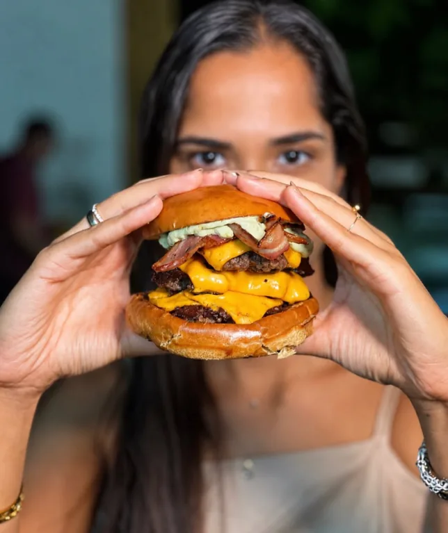 Cliente segurando um smash burger duplo com cheddar derretido e maionese verde