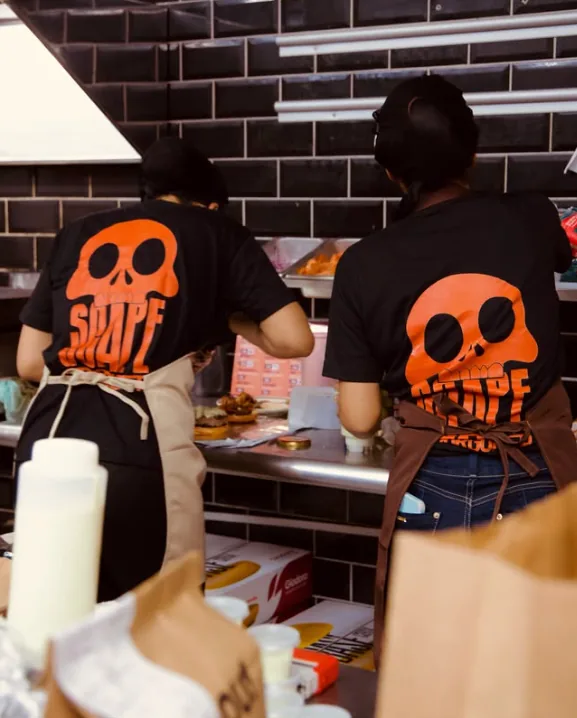 Equipe do Scape Burguer na cozinha, com camisetas pretas e a caveira laranja da marca